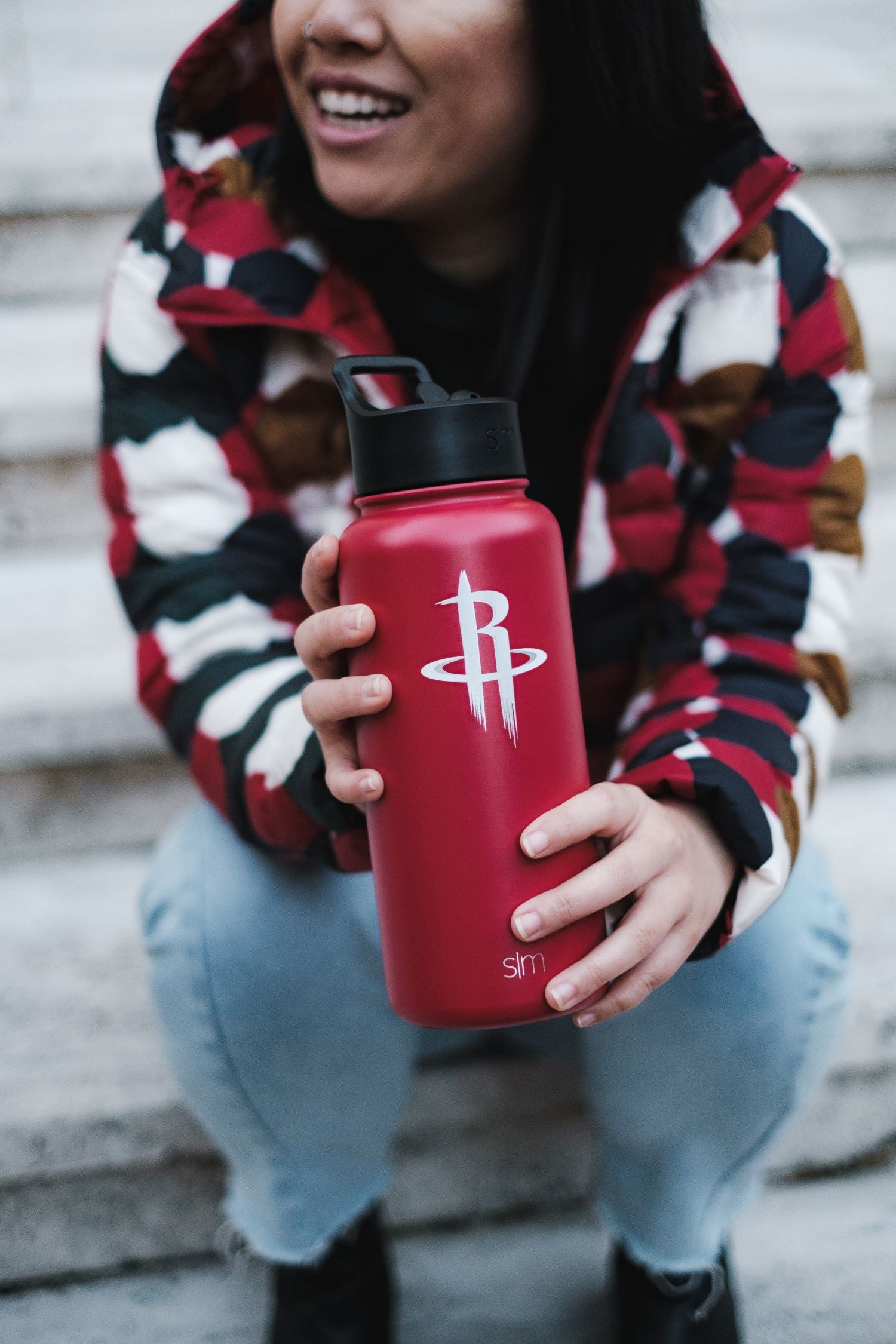 Person wearing colorful geometric patterned jacket holding bright red water bottle