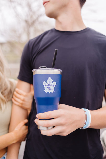 Insulated tumbler in royal blue with white lid rim and logo, held in hand against a blurred background