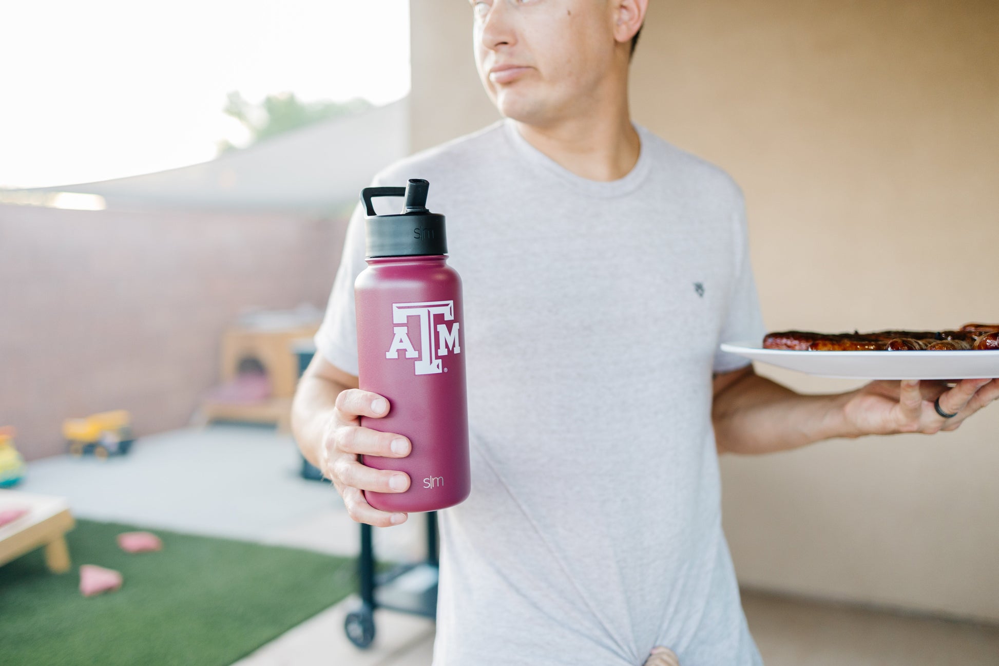 Man in light gray t-shirt holding deep burgundy water bottle against neutral background
