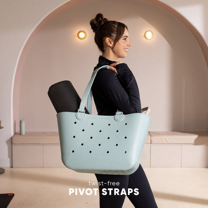 Woman in black athletic top carrying mint green Simple Modern Getaway Bag with perforated design and twist-free pivot straps in modern minimalist studio setting with arched alcove.