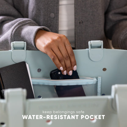 Person placing black smartphone into water-resistant pocket of sage green getaway bag. Text reads "keep belongings safe" and "WATER-RESISTANT POCKET."