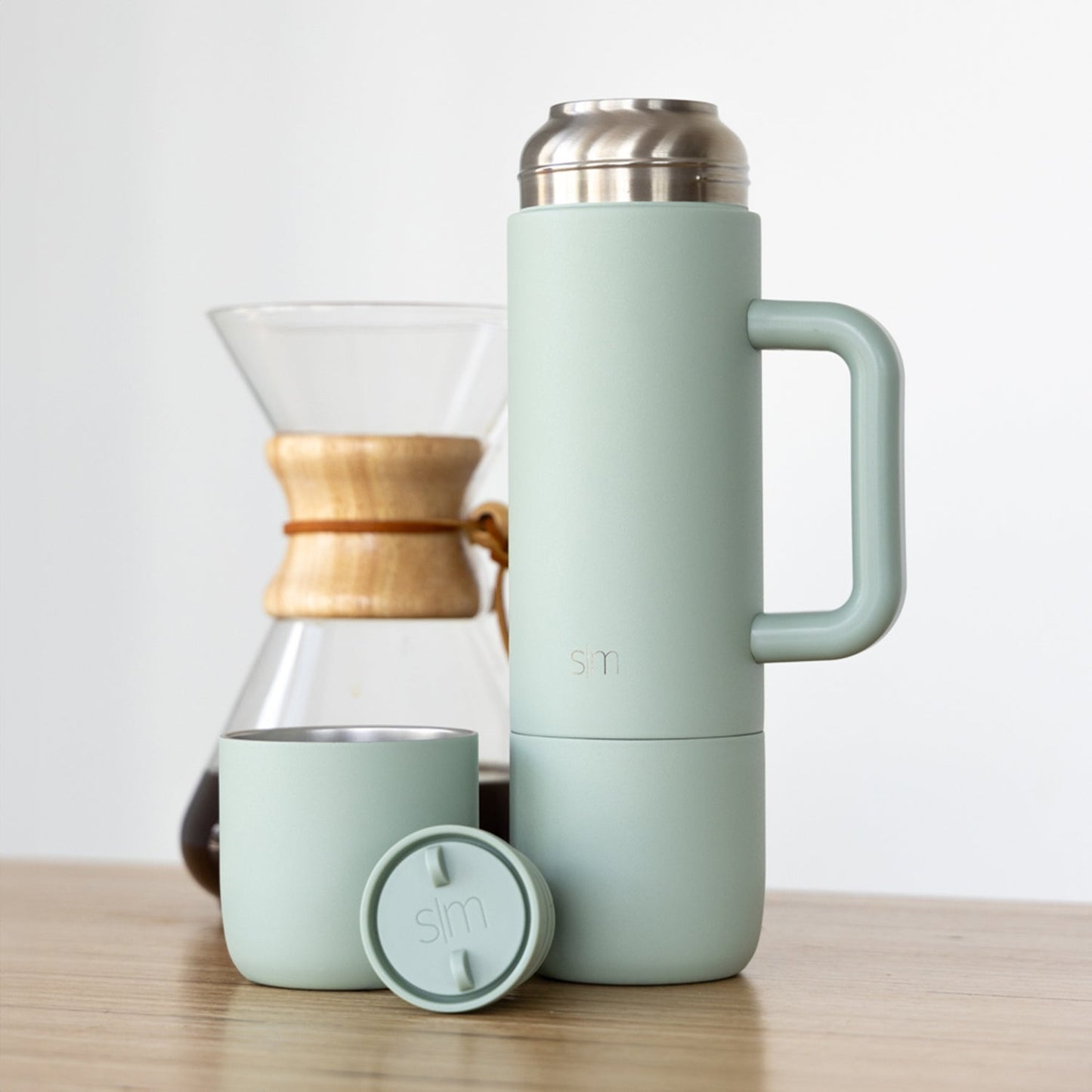 Sage green drinkware collection displayed with natural wood and stainless steel accents on a soft, neutral background