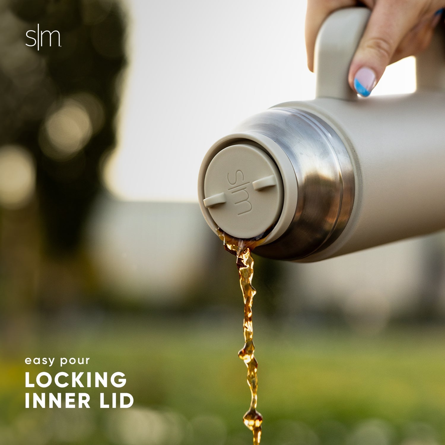 Stainless steel pitcher pouring golden amber liquid against a neutral metallic background